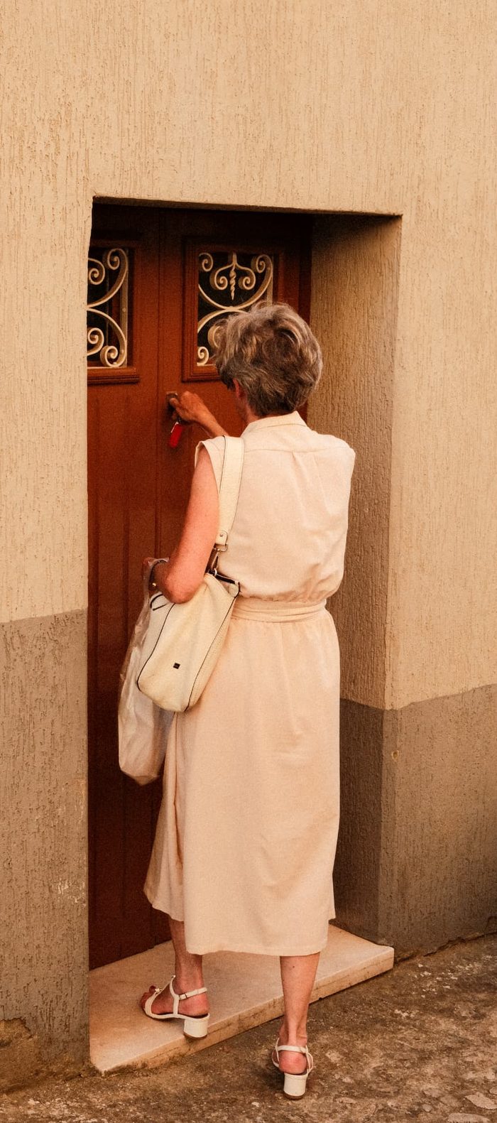 Frau im cremefarbenen Kleid schliesst in Italien eine Haustür mit einem Schlüssel auf